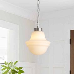 a white light hanging from a ceiling in a room next to a potted plant