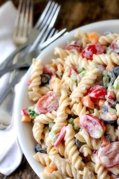 a bowl filled with pasta salad on top of a wooden table next to silverware