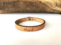 a leather bracelet with the word blggad engraved on it, sitting next to a piece of wood