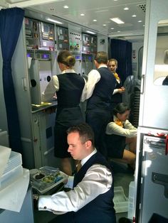 an airplane cabin with several people in the aisle and one man serving food to another person