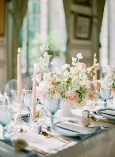 the table is set with white and pink flowers in vases, candles, and plates