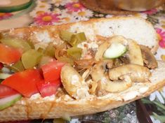 a sandwich with mushrooms, tomatoes, peppers and cucumbers on it sitting on a floral table cloth