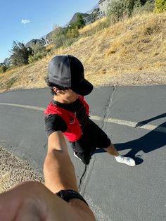 a young boy riding on the back of a skateboard down a street next to a person's hand