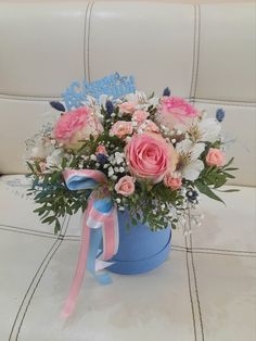 a blue bucket with pink roses and baby's breath in it sitting on a couch