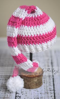 a pink and white knitted hat sitting on top of a wooden stump