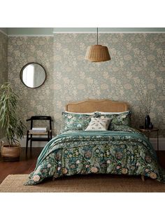 a bed in a room with a green wallpaper and wooden flooring next to a round mirror