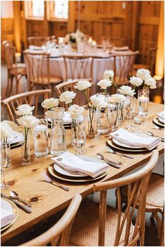 the table is set with white flowers in vases and place settings for guests to sit at