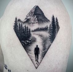 a man with a mountain scene tattoo on his back shoulder and chest is walking down a path through the woods