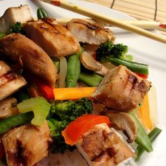 a white plate topped with meat and veggies next to chopsticks on a table