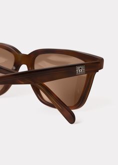 TOTEME sunglasses made in Italy with a squared acetate frame that's softened along the edges. The light brown-tinted lenses offer UV protection and can be replaced with prescription lenses, while the arms are accented with a silver-tone monogram plaque. Style them with city and vacation edits. Brown Rectangular Sunglasses With Tinted Lenses, Brown Rectangular Tinted Sunglasses, Brown Tinted Rectangular Sunglasses, Brown Acetate Sunglasses With Uv Protection, Brown Square Frame Polarized Sunglasses, Brown Square Frame Sunglasses With Polarized Lenses, Brown Acetate Cat Eye Sunglasses With Polarized Lenses, Brown Square Frame Sunglasses With Uv Protection, Modern Brown Sunglasses With Polarized Lenses