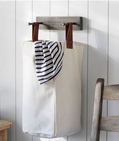 a white bag hanging on a wall next to a wooden chair and table with a black and white striped scarf