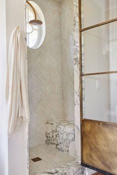 a bathroom with marble tile and wood trim on the shower wall, along with a round window