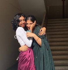 two women hugging each other in front of stairs