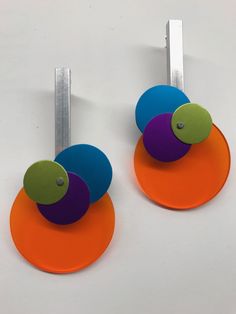 two circular earrings with colored discs attached to the back of each earring, on a white surface