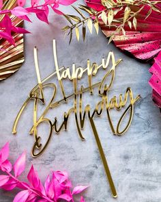 a cake topper that says happy birthday with pink flowers and leaves in the background