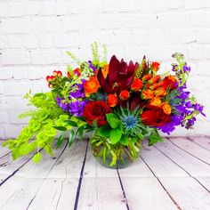 a vase filled with lots of colorful flowers on top of a wooden table next to a white brick wall