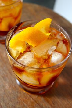 two glasses filled with ice and orange slices on top of a wooden table next to each other