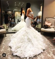 a woman in a white wedding dress is looking at herself in the mirror while others are sitting on couches