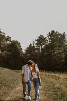 a man and woman kissing in the middle of a field with trees in the background