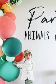 a little boy standing in front of a wall with balloons on it's side