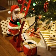 a christmas tree with presents under it and a santa clause on the ladder next to it