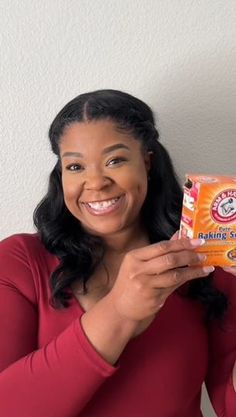 a woman is holding up a box of orange juice and smiling at the camera while wearing a red shirt