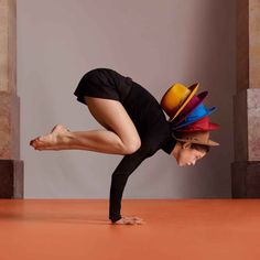 a woman is doing a handstand with hats on her head and legs in the air