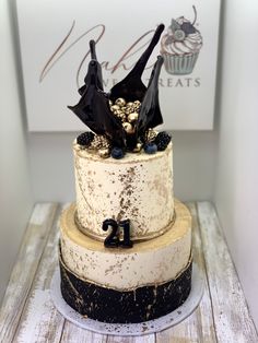 a three tiered cake decorated with black bats and gold sprinkles on a wooden table