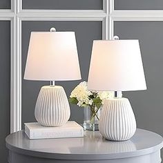 two white lamps sitting on top of a table next to a vase with flowers in it