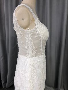 the back of a white wedding dress on a mannequin head stand in front of a curtain