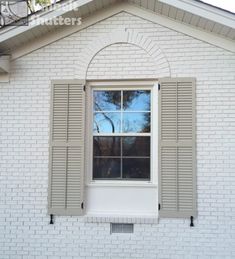 a white brick house with shutters open and trees in the window sill behind it