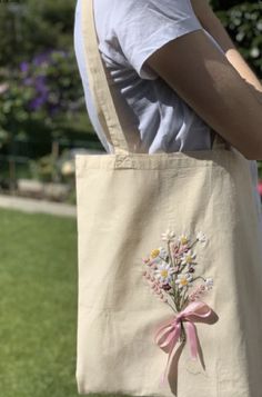 a person holding a bag with flowers on it and a pink ribbon around the handle