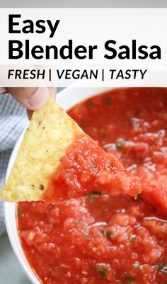 a hand holding a tortilla chip and dipping it into a bowl of salsa