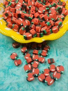 red and green beads are in a yellow bowl on a blue tablecloth next to a yellow plate