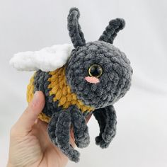 a hand holding a small gray and yellow crocheted stuffed animal with white wings