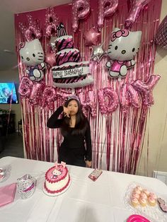 a woman standing in front of a table with pink balloons and hello kitty decorations on it