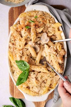 a person holding a fork in a bowl of pasta with mushrooms and spinach on the side