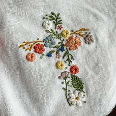 an embroidered cross on top of a white cloth with flowers and leaves in the center