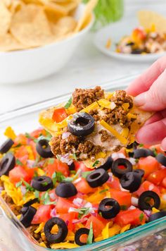 a hand holding a tortilla chip with black olives, cheese and other toppings