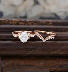 two wedding rings with diamond accents on top of each other, sitting on a wooden surface