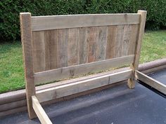 a bed frame made out of wood sitting on top of a tarmac next to some bushes