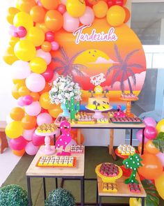 an assortment of desserts on tables in front of a wall decorated with balloons and palm trees