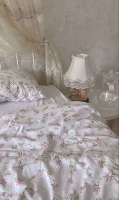 a white bed with pink flowers on the comforter and two night stands next to it