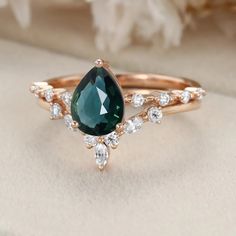 a close up view of a ring with a pear shaped green stone surrounded by white diamonds