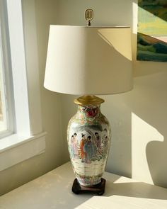 a lamp sitting on top of a white table next to a window with a painting on it