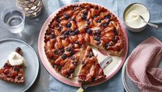 a pie with blueberries and strawberries is on a plate next to some glasses