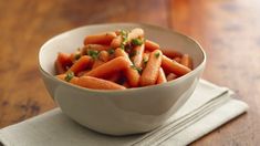 a white bowl filled with carrots sitting on top of a wooden table next to a napkin