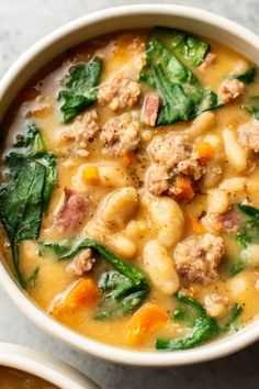 two bowls of soup with meat, spinach and carrots on the side next to each other