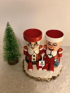 two red and white ceramic vases sitting on top of a wooden stump next to a small christmas tree