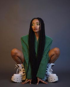 a woman sitting on the ground with her legs crossed wearing white sneakers and green sweater